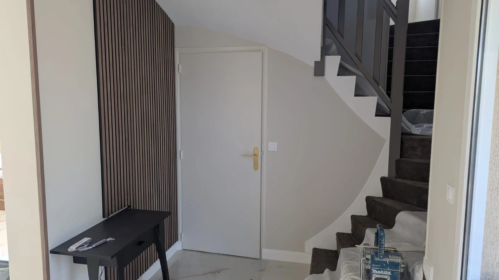 Entrée aux murs clairs avec panneau à tasseaux et escalier peint en gris foncé.
