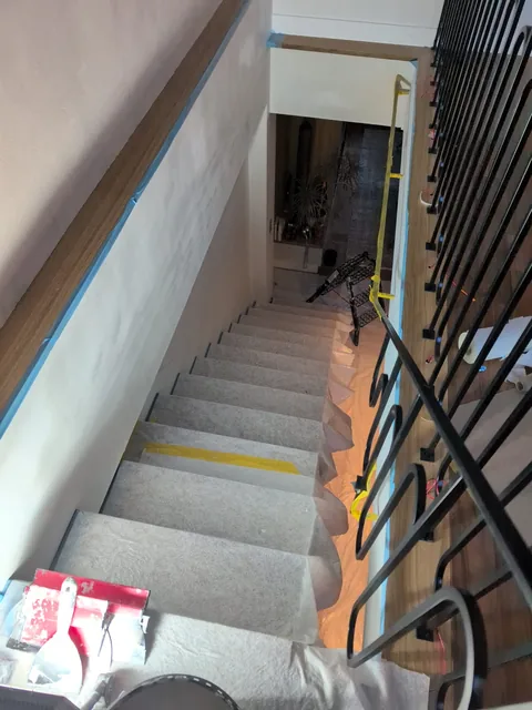 Cage d’escalier protégée par des bâches et rubans de masquage pendant la mise en peinture des murs.