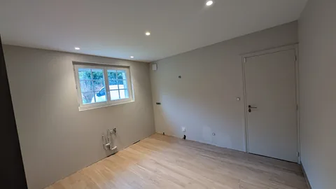 Pièce vide aux murs gris clair, plafond blanc à spots et sol bois clair, avec arrivées techniques en attente.