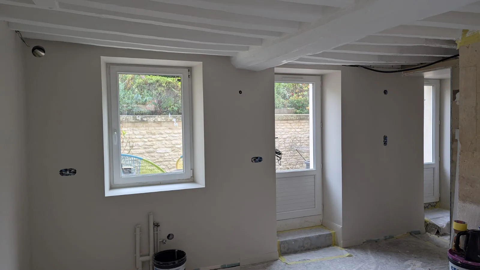 Pièce avec murs gris, encadrements blancs et poutres de plafond peintes en blanc.