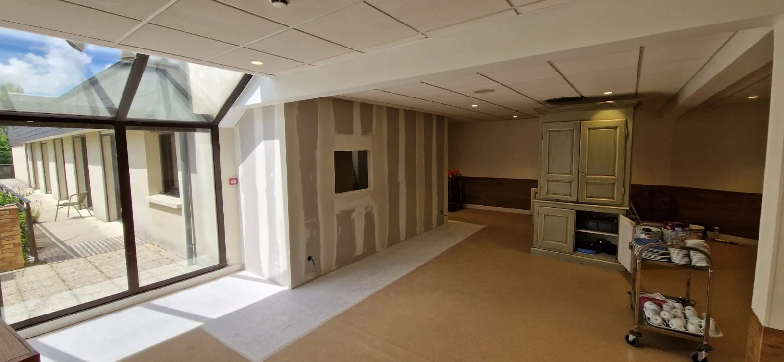 Grande pièce vitrée avec cloison et plafond en plaques de plâtre aux bandes de joints apparentes.