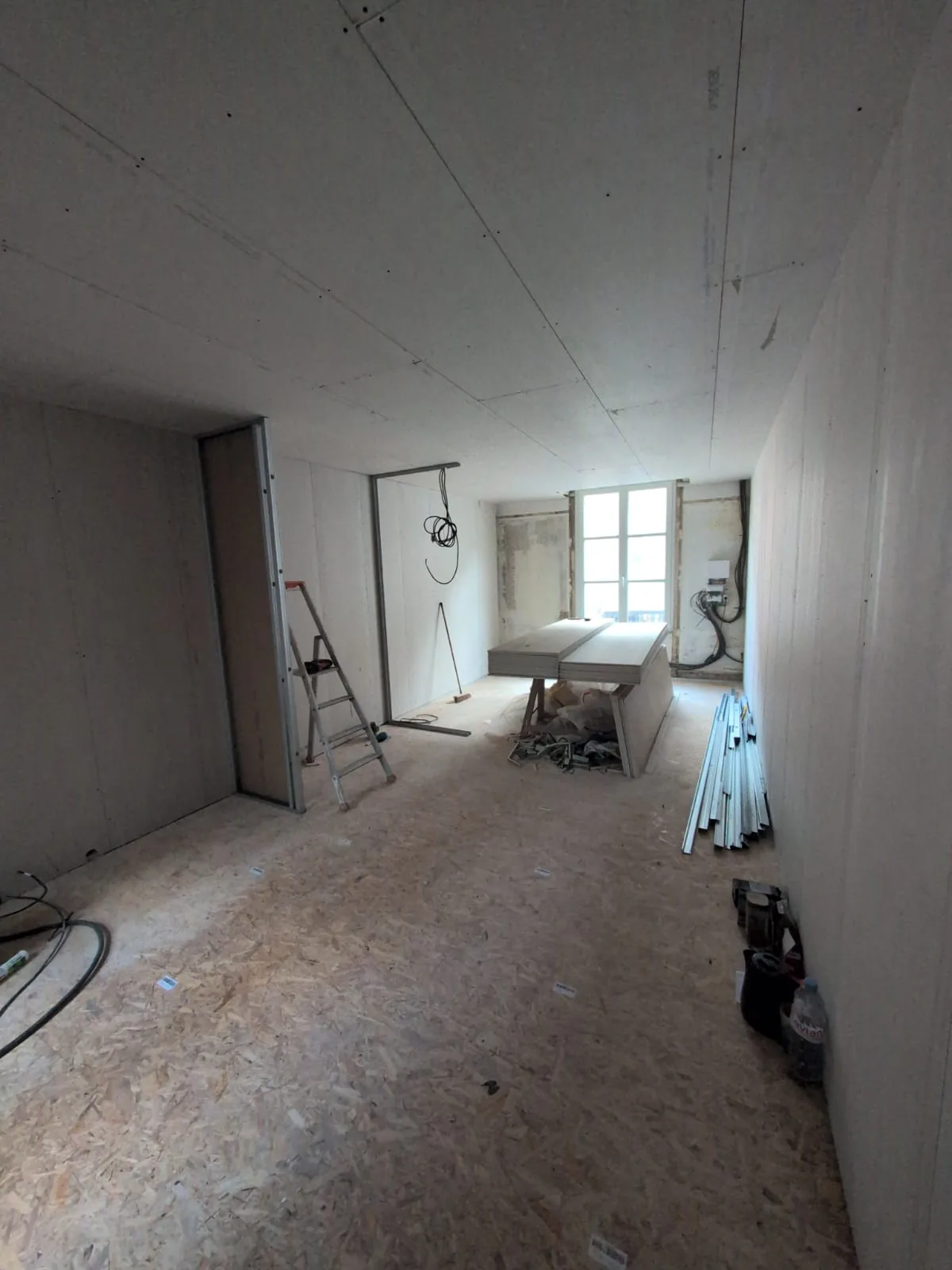 Pièce en chantier habillée de plaques de plâtre, avec ossatures métalliques et plaques empilées.