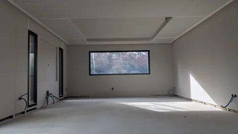 Grande pièce brute habillée de plaques de plâtre, avec plafond à décroché et joints non terminés.