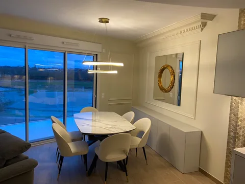 Salle à manger claire ornée de cadres muraux et d'une corniche à denticules autour d'un grand miroir.