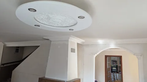 Plafond décoré d’un caisson circulaire à rosace et spots, avec corniches et arcade moulurée.