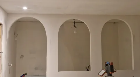 Cloison blanche composée de trois grandes arcades arrondies avec finitions encore visibles.